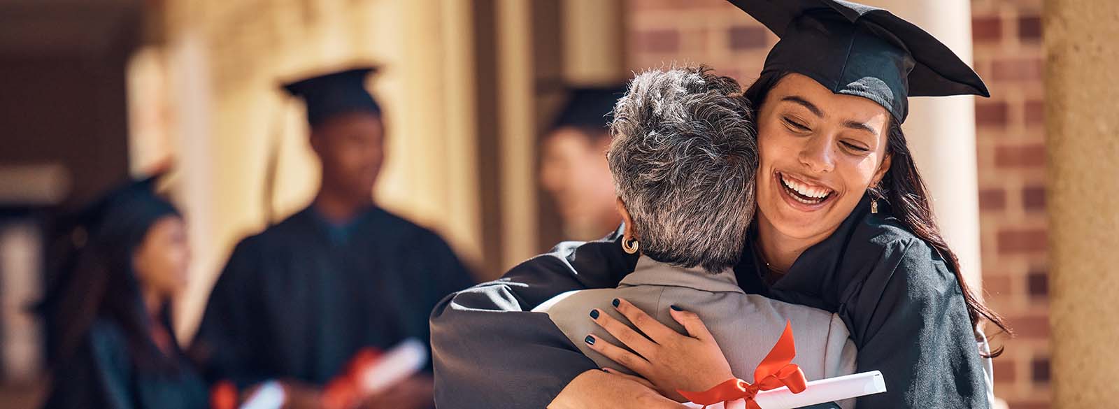 Student graduate hugging a person with other graduates nearby
