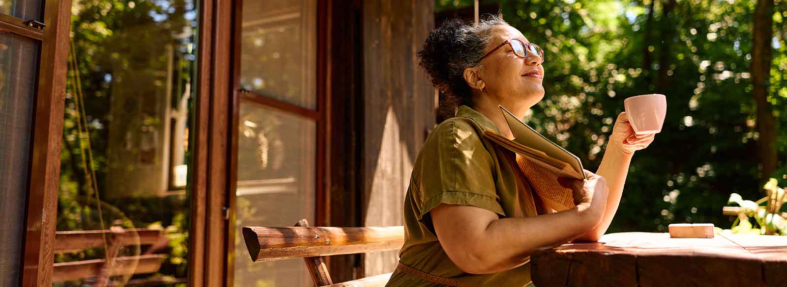 Person smiling on porch while holding mug and book