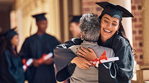 Student graduate hugging a person with other graduates nearby