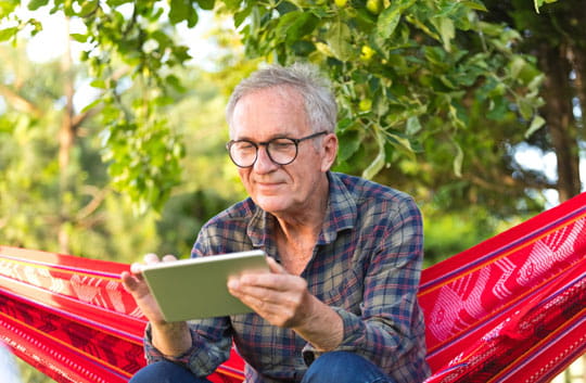 Older gentleman sitting in hammock and using a tablet