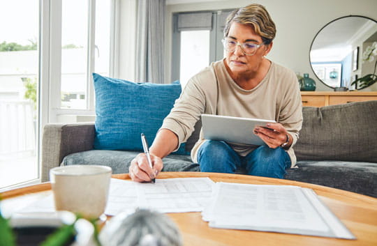 Woman reviews paperwork while looking at tablet
