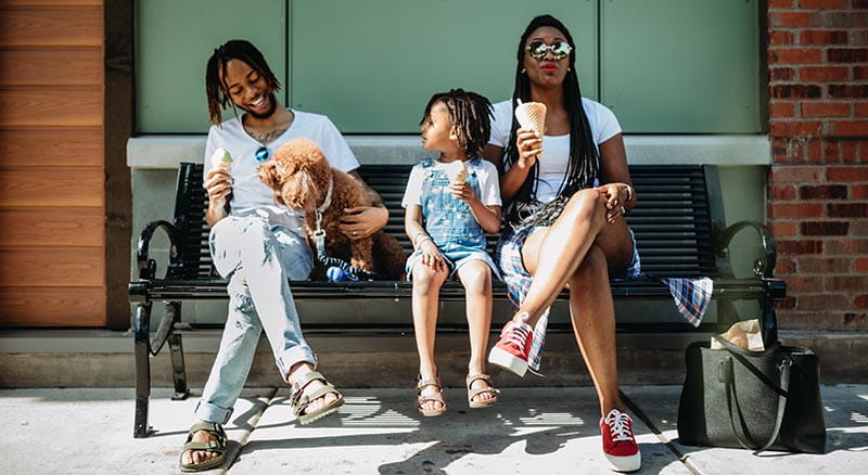 Man petting dog on bench with young child and woman