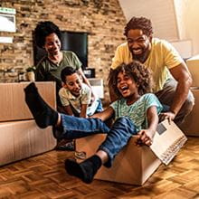 Parents pushing children in moving boxes on the floor