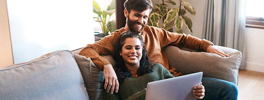 Couple relaxing on sofa looking at laptop